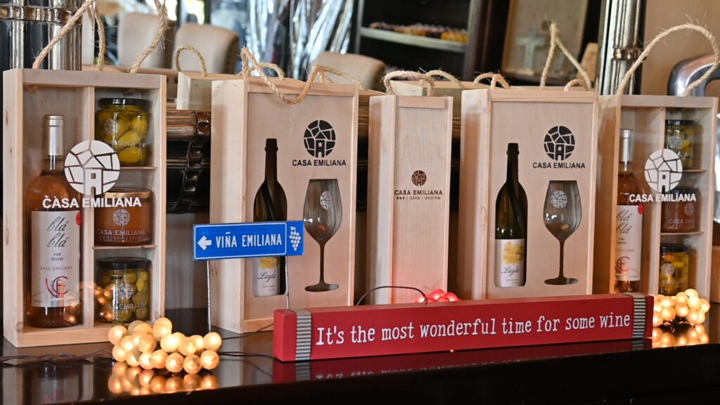 Botellas de vino de Casa Emiliana en exhibición en el mostrador de degustación, Valle de Guadalupe, con etiquetas de Syrah y Nebbiolo, ambiente de vinícola boutique.